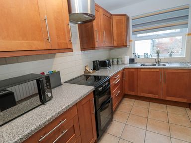 A kitchen with wooden cabinets a microwave stove and a window with striped blind at The Haven in North Sunderland near Seahouses