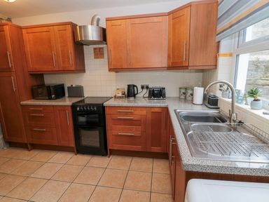 A kitchen with wooden cabinets a black stove a silver sink and countertop appliances at The Haven in North Sunderland near Seahouses