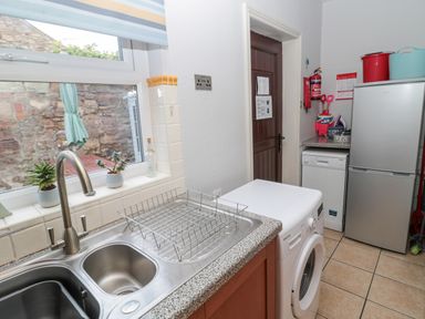 A utility room with a double sink dish rack washing machine refrigerator and door at The Haven in North Sunderland near Seahouses