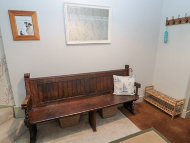 A hallway with a wooden bench and a cushion a wooden shoe rack and coat hooks at The Haven in North Sunderland near Seahouses