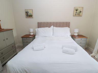 A bedroom with a double bed white bedding bedside tables lamps and a dresser at The Haven in North Sunderland near Seahouses