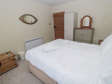 A bedroom with a bed towels a wooden chest a wardrobe a cabinet with a mirror and a wooden door at The Haven in North Sunderland near Seahouses