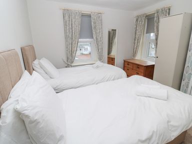 A bedroom with two single beds white bedding wooden dresser full length mirror and two windows with curtains at The Haven in North Sunderland near Seahouses