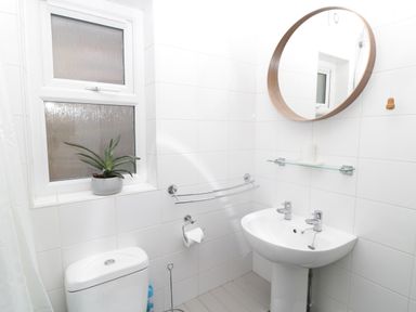 A bathroom with a toilet a sink a round mirror and a plant on the window sill at The Haven in North Sunderland near Seahouses