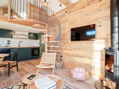 A living area with a wooden spiral staircase kitchen cabinets and a wood burning stove at Little Beach Cabin in Crantock