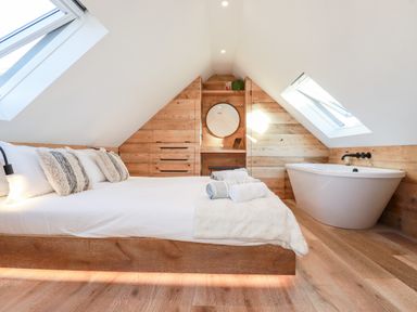 A bedroom with a bed pillows folded towels a bathtub and built in wooden cabinetry with skylights at Little Beach Cabin in Crantock