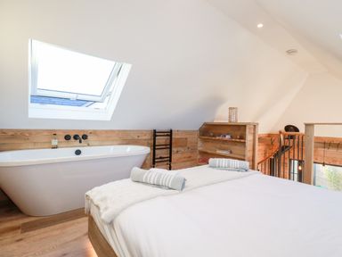 A bedroom with a bathtub under a skylight window and wooden shelving at Little Beach Cabin in Crantock