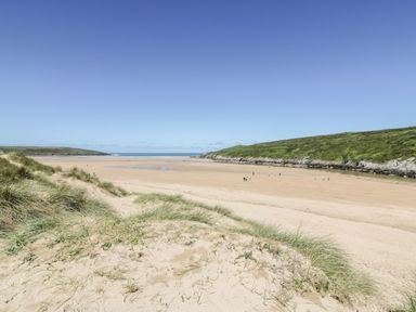A sandy beach with grass-covered dunes and people walking near the water at Little Beach Cabin in Crantock