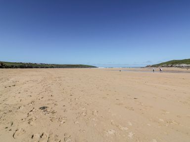 A wide sandy beach with footprints and people walking near the water at Little Beach Cabin in Crantock