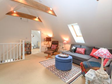 An attic lounge with a brown armchair a grey sofa with cushions and a blue ottoman on a patterned rug at The Hayloft in Haddiscoe
