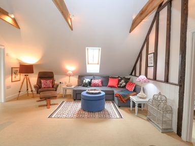 A living room with a gray sectional sofa a blue ottoman a brown recliner and decorative lamps at The Hayloft in Haddiscoe