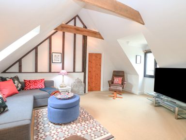 An attic living room with a gray sectional sofa and colorful pillows and a blue ottoman on a patterned rug at The Hayloft in Haddiscoe