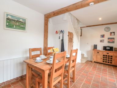 A dining area with a wooden table and four chairs set with cups and plates near a staircase and a wooden sideboard at The Hayloft in Haddiscoe