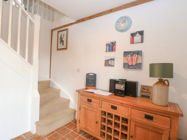 Staircase with beige carpet beside wooden cabinet with stereo lamp and wall clock at The Hayloft in Haddiscoe