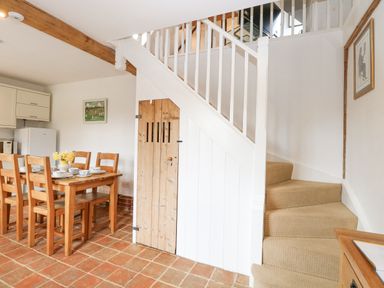 A dining area with wooden table and chairs next to a staircase with a wooden door under it at The Hayloft in Haddiscoe
