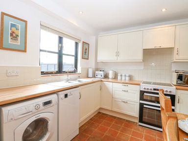 A kitchen with white cabinets wooden countertops washing machine dishwasher oven and a window at The Hayloft in Haddiscoe