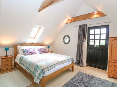 A bedroom with a wooden bed and side tables under a skylight window and a black door at The Hayloft in Haddiscoe