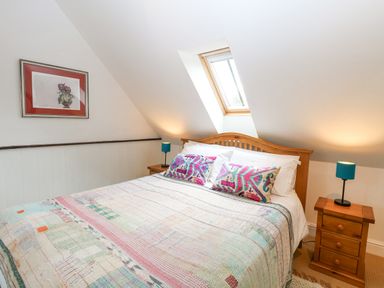 A bedroom with a wooden bed under a skylight and two side tables with lamps at The Hayloft in Haddiscoe