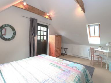 A bedroom with a bed a wooden wardrobe a desk with a chair and a window at The Hayloft in Haddiscoe