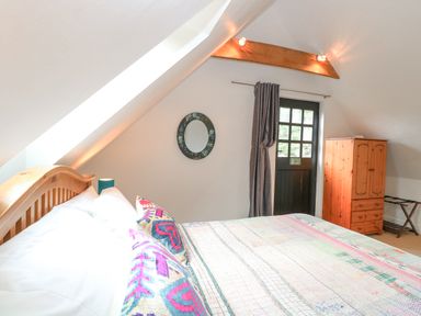 A bedroom with a wooden bed a colorful quilt a wall mirror a dark door a wooden wardrobe and a luggage rack at The Hayloft in Haddiscoe