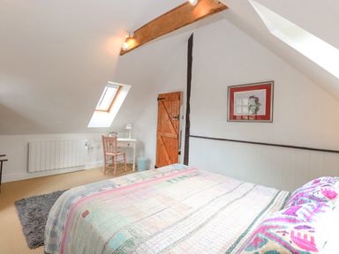 A bedroom with a bed covered in a multicolored quilt a small white desk with a chair under a skylight and a wooden door at The Hayloft in Haddiscoe