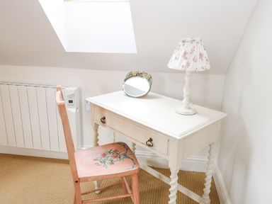 A white desk with a floral lamp and a small mirror with a pink floral chair beside a radiator in a room with a skylight at The Hayloft in Haddiscoe