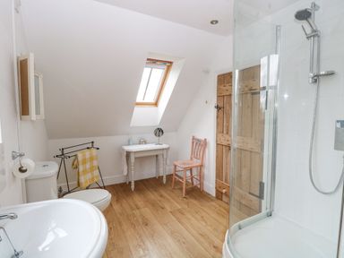 A bathroom with a shower enclosure sink toilet wooden floor small table and chair at The Hayloft in Haddiscoe