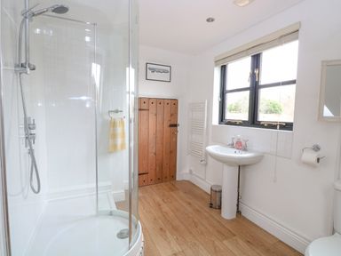 A bathroom with a curved glass shower enclosure wooden door white pedestal sink and window at The Hayloft in Haddiscoe
