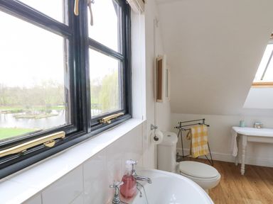 A bathroom with a sink and toilet by windows overlooking a pond and trees at The Hayloft in Haddiscoe