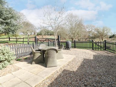 A fenced outdoor patio area with a round table and four wicker chairs and a covered barbecue grill at The Hayloft in Haddiscoe