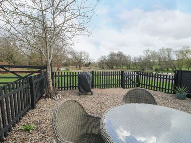 An outdoor patio area with a glass table and wicker chairs enclosed by a black picket fence at The Hayloft in Haddiscoe