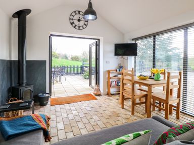 A living area with wooden dining table and chairs a wood stove and open patio doors at The Grain Store in Haddiscoe