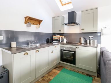 A kitchen with gray cabinets a black oven and stove a wooden shelf and a green rug at The Grain Store in Haddiscoe