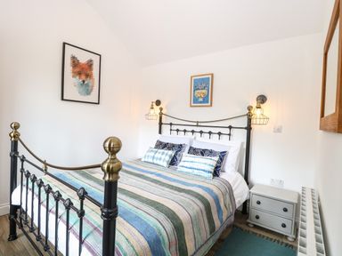 A bedroom with a metal bed frame striped blanket pillows wall art bedside table and lamps at The Grain Store in Haddiscoe