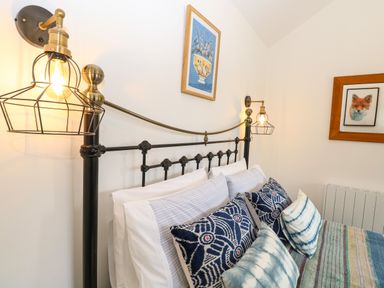A bed with patterned cushions and striped pillows under wall lamps and framed artwork at The Grain Store in Haddiscoe