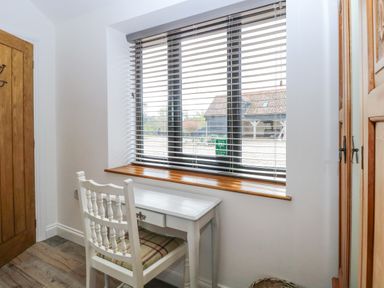A small white desk with a chair by a window with blinds in a room with wooden door and wardrobe at The Grain Store in Haddiscoe
