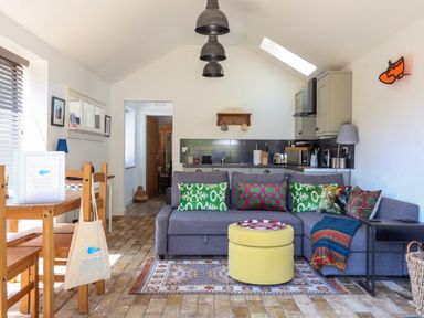 A living area with a gray sofa and colorful cushions next to a small kitchen and dining table at The Grain Store in Haddiscoe