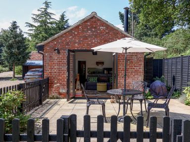 A brick house with open doors leading to a patio with a table umbrella and metal chairs at The Grain Store in Haddiscoe