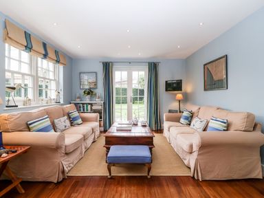 A living room with two beige sofas a wooden coffee table and a blue footstool at Lampland House in Walberswick
