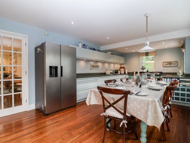 A kitchen with a dining table set for a meal and a stainless steel refrigerator at Lampland House in Walberswick