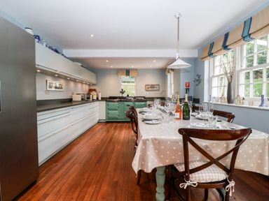 A kitchen with a dining table set with plates glasses and bottles beside windows at Lampland House in Walberswick