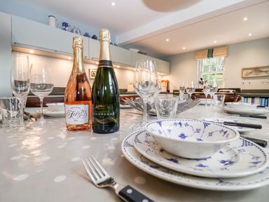 A dining table set with plates bowls cutlery and glasses with two bottles of wine in a kitchen at Lampland House in Walberswick