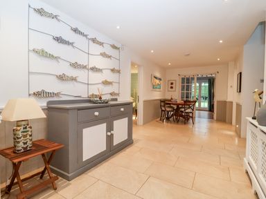 A hallway with a gray and white cabinet wall art of fish and a dining table with chairs at Lampland House in Walberswick