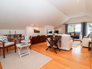 A living room with wooden chairs a white table white sofas blue and white cushions and a bookshelf at Lampland House in Walberswick