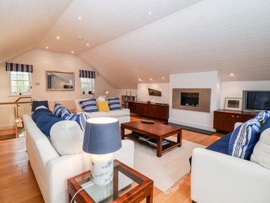 A living room with white sofas and striped pillows a wooden coffee table and a wall-mounted fireplace at Lampland House in Walberswick