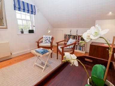 A sitting area with two wooden chairs and cushions a small table with books a window with a striped curtain and a bookshelf at Lampland House in Walberswick