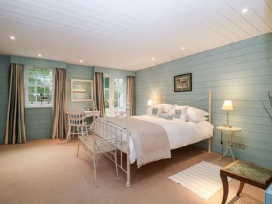 A bedroom with a bed a bench a chair two windows and a door at Lampland House in Walberswick