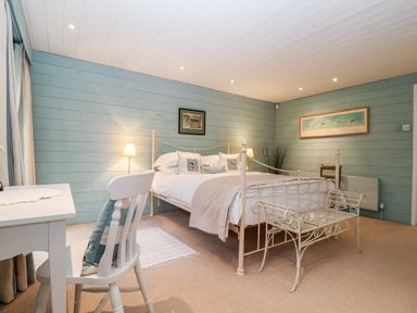 A bedroom with a white metal bed frame a white desk and chair and light blue wooden walls at Lampland House Walberswick