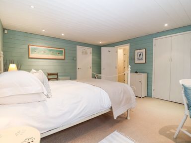 A bedroom with a bed pillows and blanket a chair artwork on the walls and a doorway at Lampland House in Walberswick