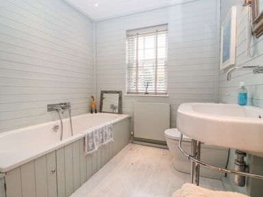 A bathroom with a bathtub a sink a toilet a window with blinds and a towel hanging on the bathtub at Lampland House in Walberswick